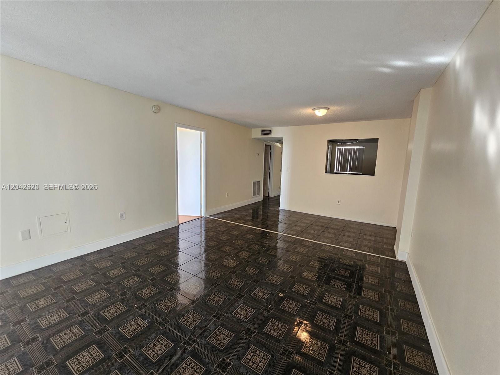An empty room features dark patterned tile flooring, light-colored walls, and a small interior window — 15600 NW 7th Ave # 704, Miami FL 33169, MIAMI, FL