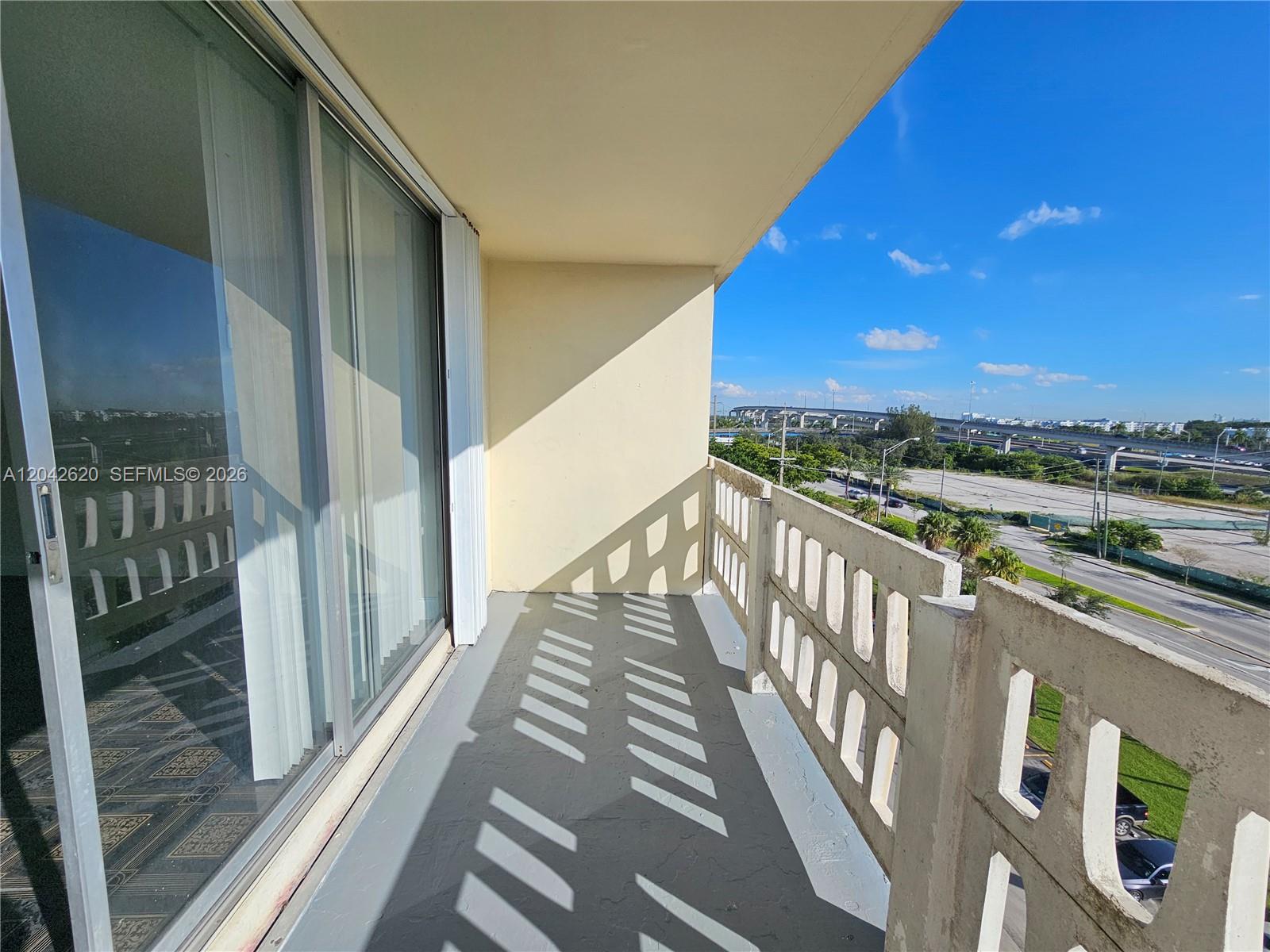 A balcony with a concrete railing overlooks a road and highway under a blue sky — 15600 NW 7th Ave # 704, Miami FL 33169, MIAMI, FL