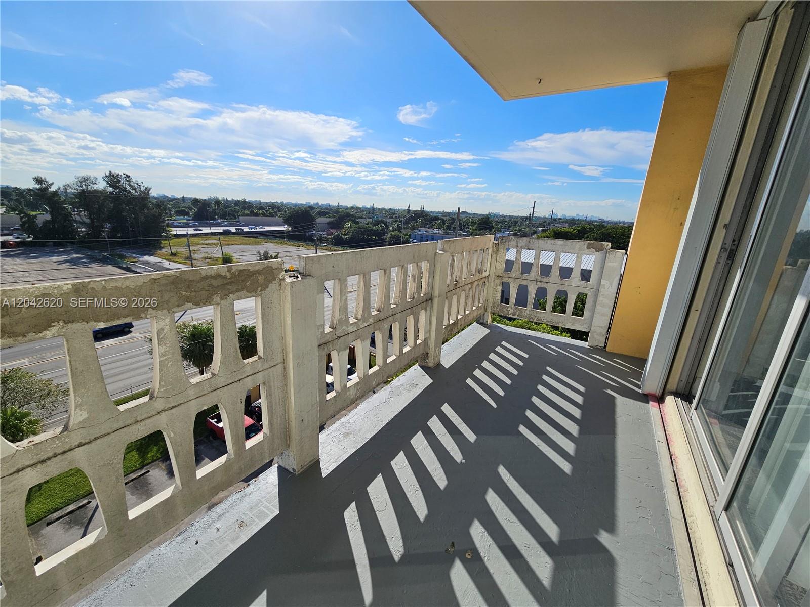 A balcony with a concrete railing overlooks a parking lot and a distant city skyline — 15600 NW 7th Ave # 704, Miami FL 33169, MIAMI, FL