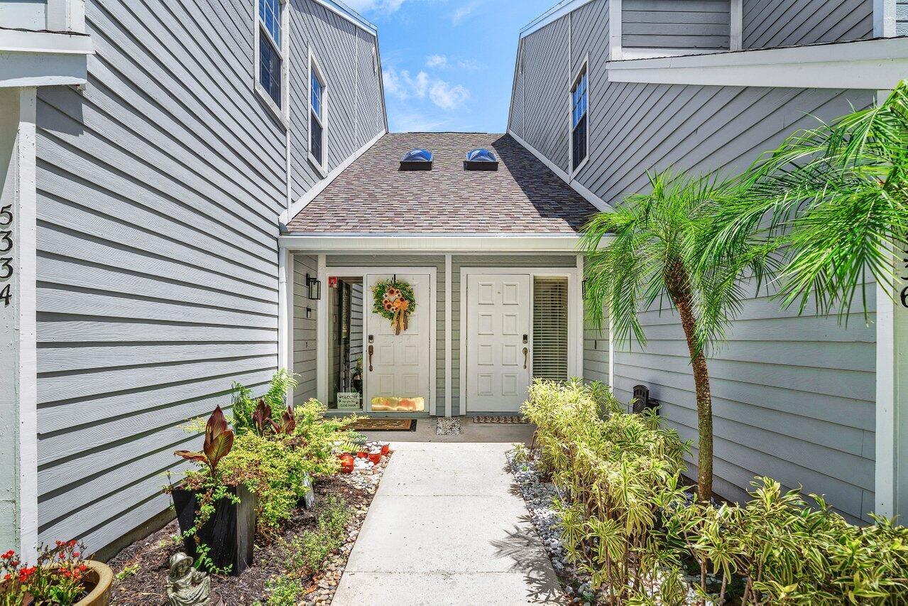 A concrete walkway leads to the side-by-side front entrances of a gray-sided duplex — 5336 Buckhead Circle # 2020, Boca Raton FL 33486, BOCA RATON, FL