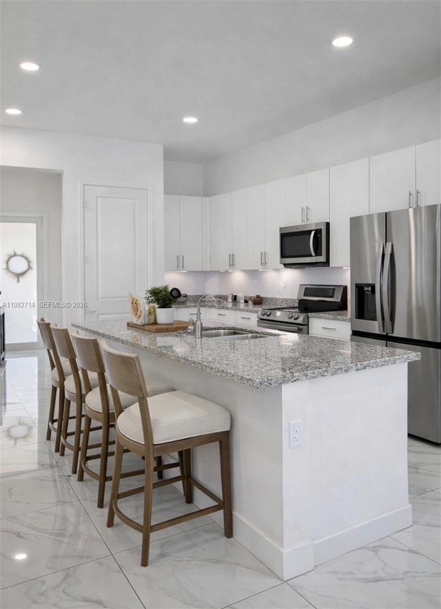 A modern kitchen features white cabinetry, granite countertops, a central island, and stainless steel appliances — 22255 SW 132nd Ave, Miami FL 33170, MIAMI, FL