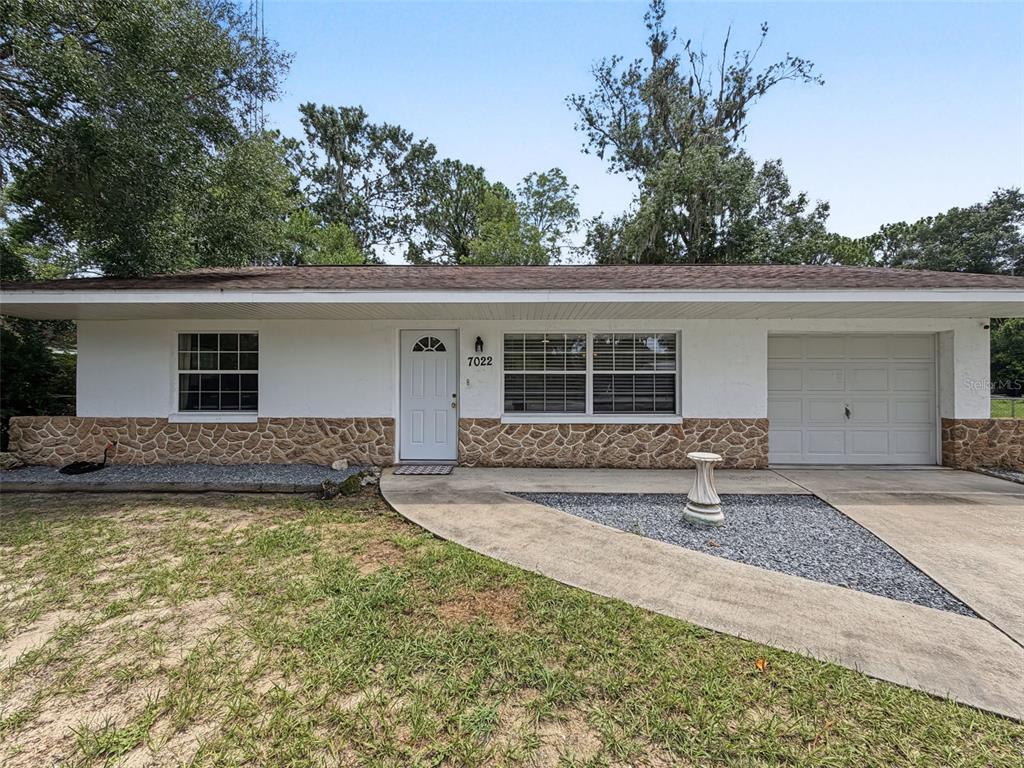 A single-story house with white siding, stone veneer, a front door, and an attached garage — 7022 W CRESTVIEW LANE, CRYSTAL RIVER, FL