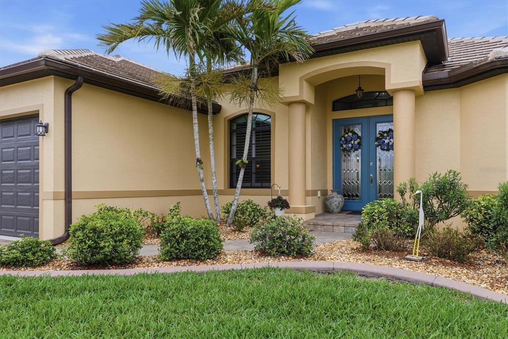 The exterior of a tan house features a blue double front door and palm trees — 15260 LEIPZIG CIRCLE, PORT CHARLOTTE, FL