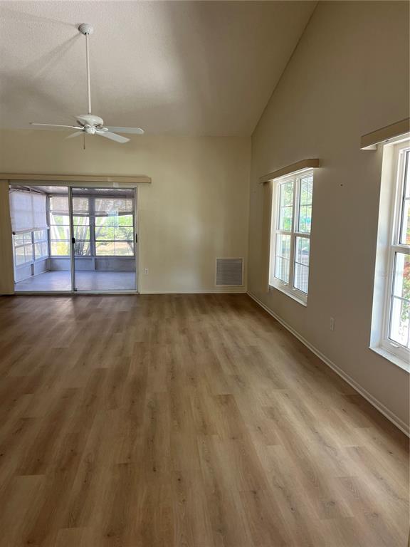 An empty living room features light wood-look flooring, a vaulted ceiling, and a sliding glass door — 2387 BENTLEY DRIVE, PALM HARBOR, FL