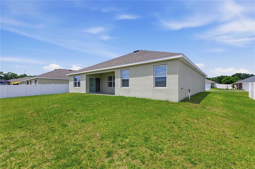 The exterior rear view of a single-story house with a lawn and white vinyl fence — 3902 SE 99TH STREET, BELLEVIEW, FL