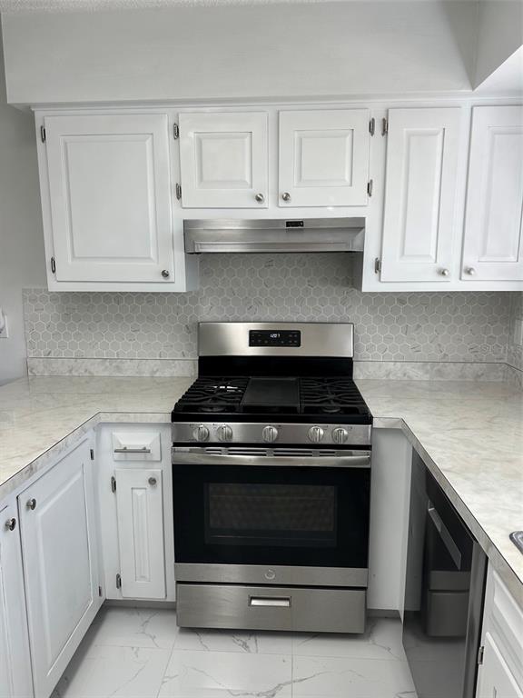A kitchen features white cabinets, a stainless steel gas range, and a hexagonal tile backsplash — 470 LAKE ROAD, OCALA, FL