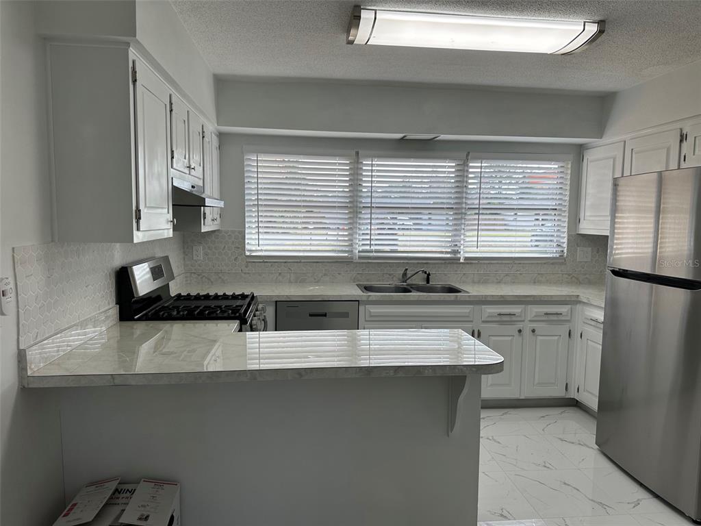 A kitchen features white cabinets, marble-look countertops, stainless steel appliances, and light-colored tile flooring — 470 LAKE ROAD, OCALA, FL