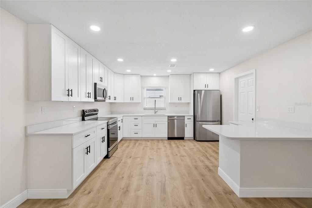 A modern kitchen features white cabinets, stainless steel appliances, quartz countertops, and light wood flooring — 6003 TAMPA SHORES BOULEVARD, TAMPA, FL