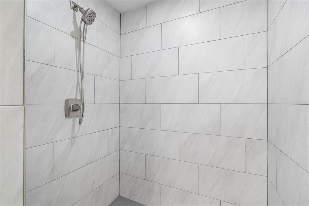 A shower stall features white marble-look subway tiles and a handheld shower head — 6003 TAMPA SHORES BOULEVARD, TAMPA, FL