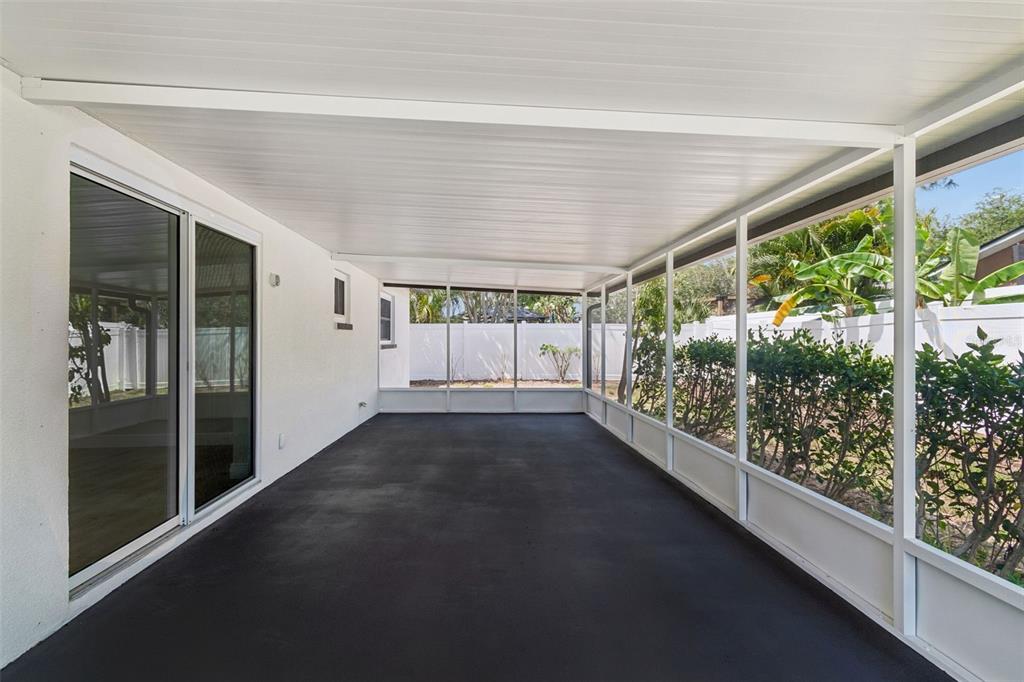 A covered, screened-in patio features a dark painted concrete floor and white structural framing — 6003 TAMPA SHORES BOULEVARD, TAMPA, FL