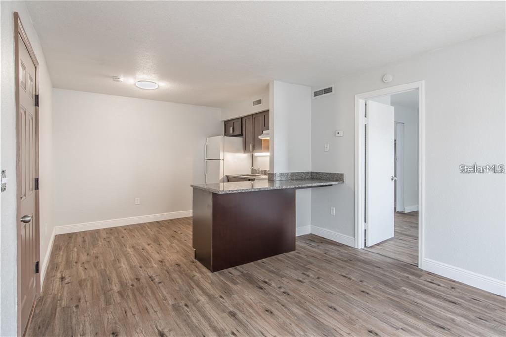 An open-concept kitchen features dark wood cabinets, granite countertops, and wood-look flooring — 9013 WESTCHESTER CIRCLE 29 APT E, TAMPA, FL
