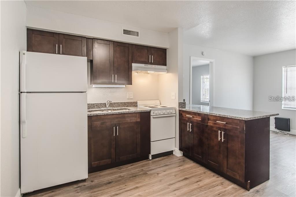 A kitchen features dark wood cabinets, granite countertops, white appliances, and light wood-look flooring — 9013 WESTCHESTER CIRCLE 29 APT E, TAMPA, FL