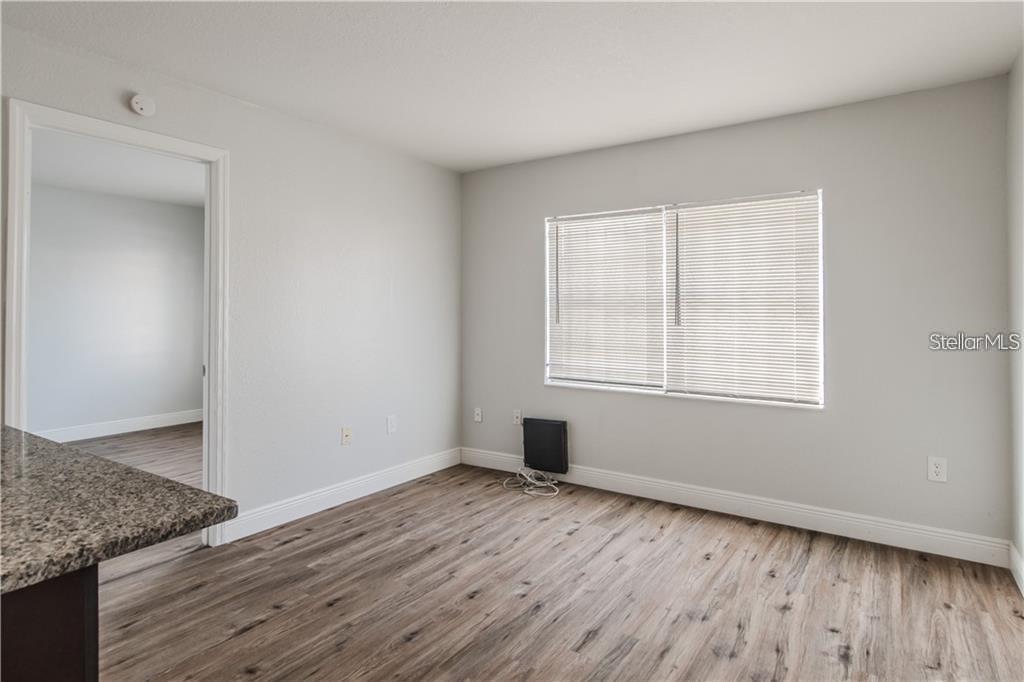 An empty room features light gray walls, wood-look flooring, a window with blinds, and a doorway — 9013 WESTCHESTER CIRCLE 29 APT E, TAMPA, FL