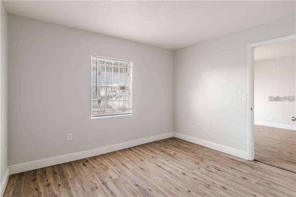 An empty bedroom features light gray walls, wood-look flooring, and a single window with blinds — 9013 WESTCHESTER CIRCLE 29 APT E, TAMPA, FL