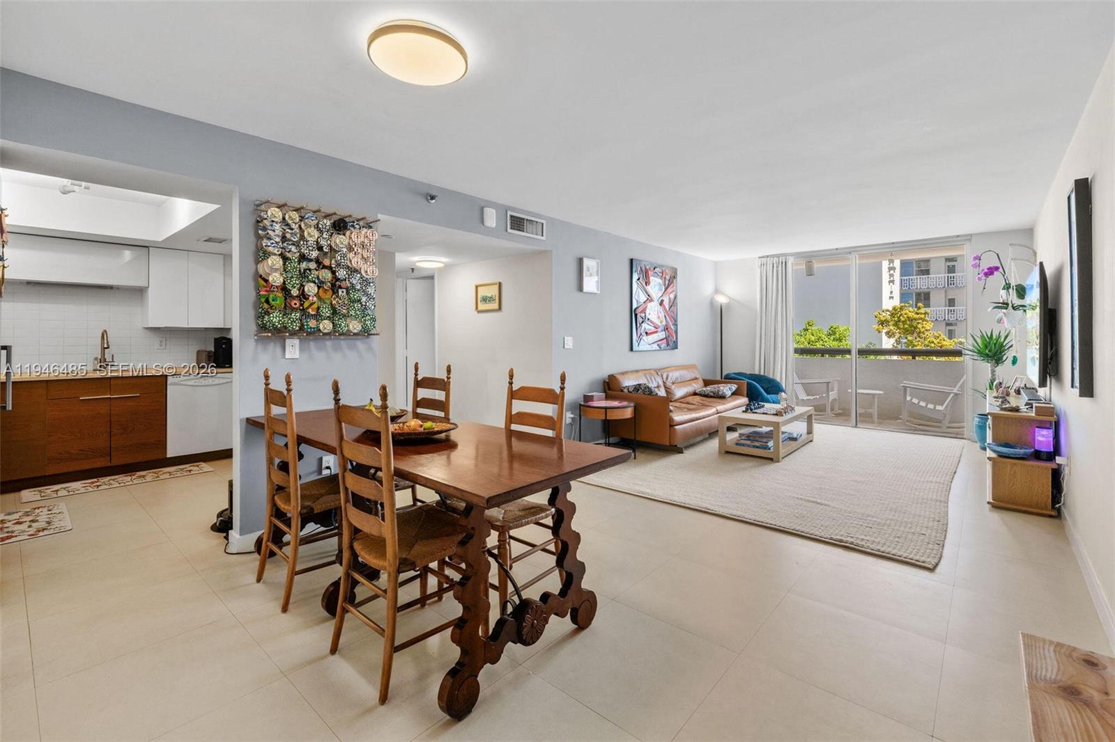 An open-concept living and dining area features tile flooring, a wooden table, and a balcony — 1775 Washington Ave # 4C, Miami Beach FL 33139, MIAMI BEACH, FL
