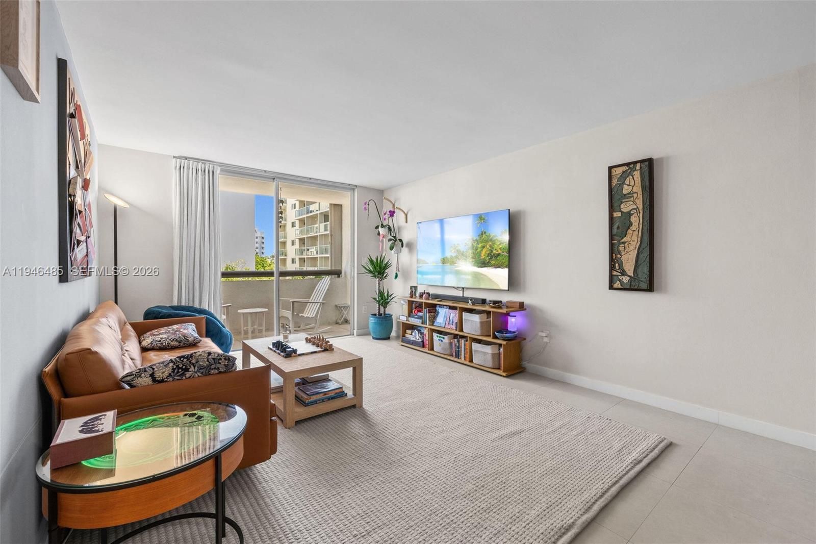 A living room features a brown sofa, a television, and a balcony with outdoor seating — 1775 Washington Ave # 4C, Miami Beach FL 33139, MIAMI BEACH, FL