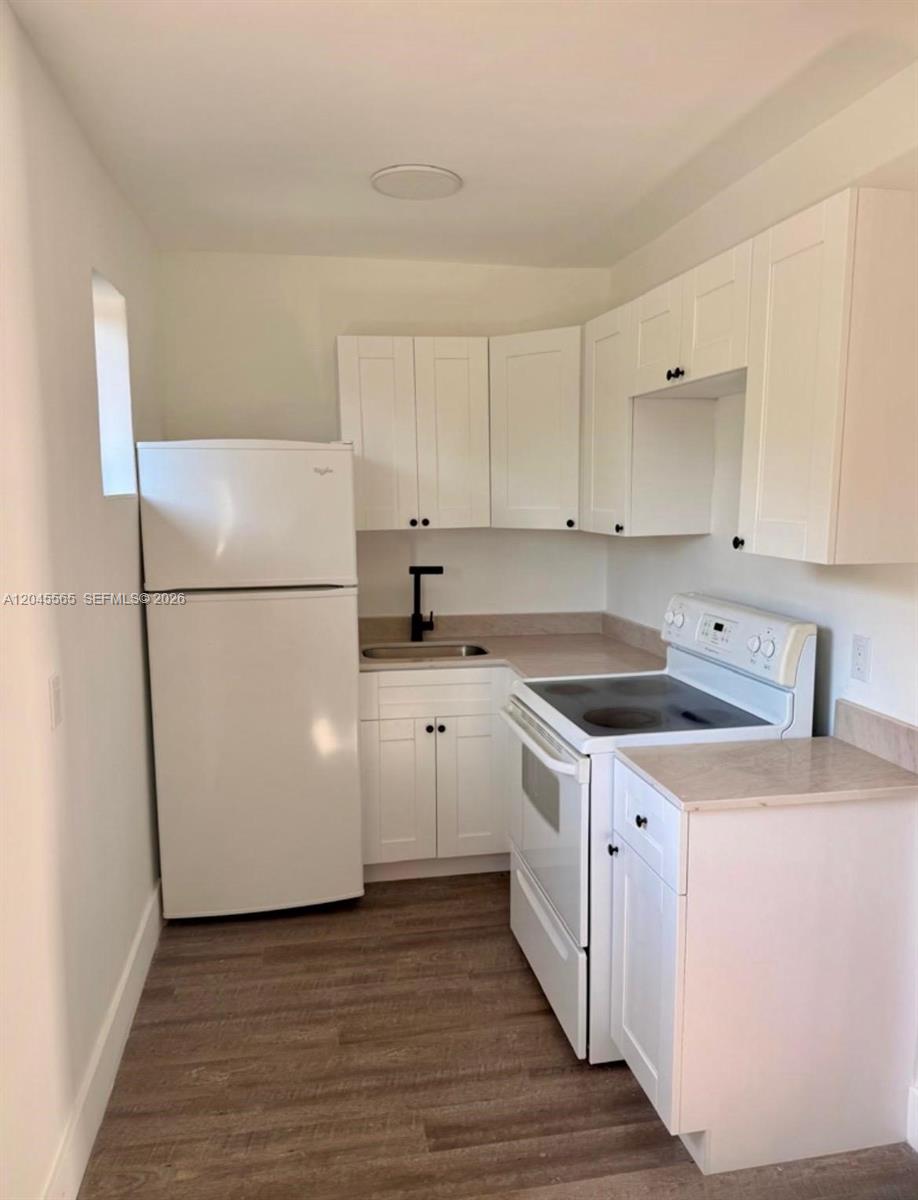 A small kitchen features white cabinets, a white refrigerator, a white stove, and wood-look flooring — 7535 NE 2nd Ct # 4, Miami FL 33138, MIAMI, FL