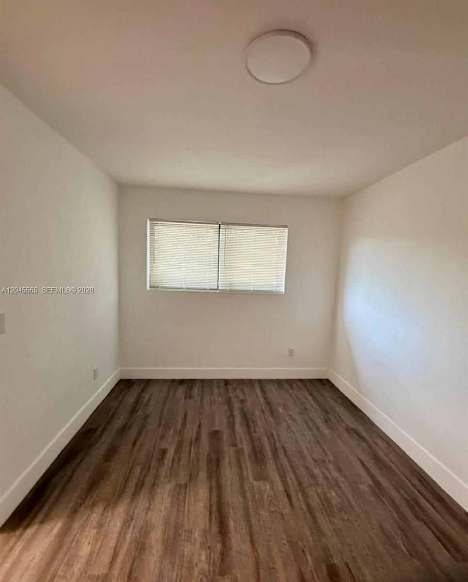 An empty room features white walls, a single window with blinds, and dark wood-look flooring — 7535 NE 2nd Ct # 4, Miami FL 33138, MIAMI, FL