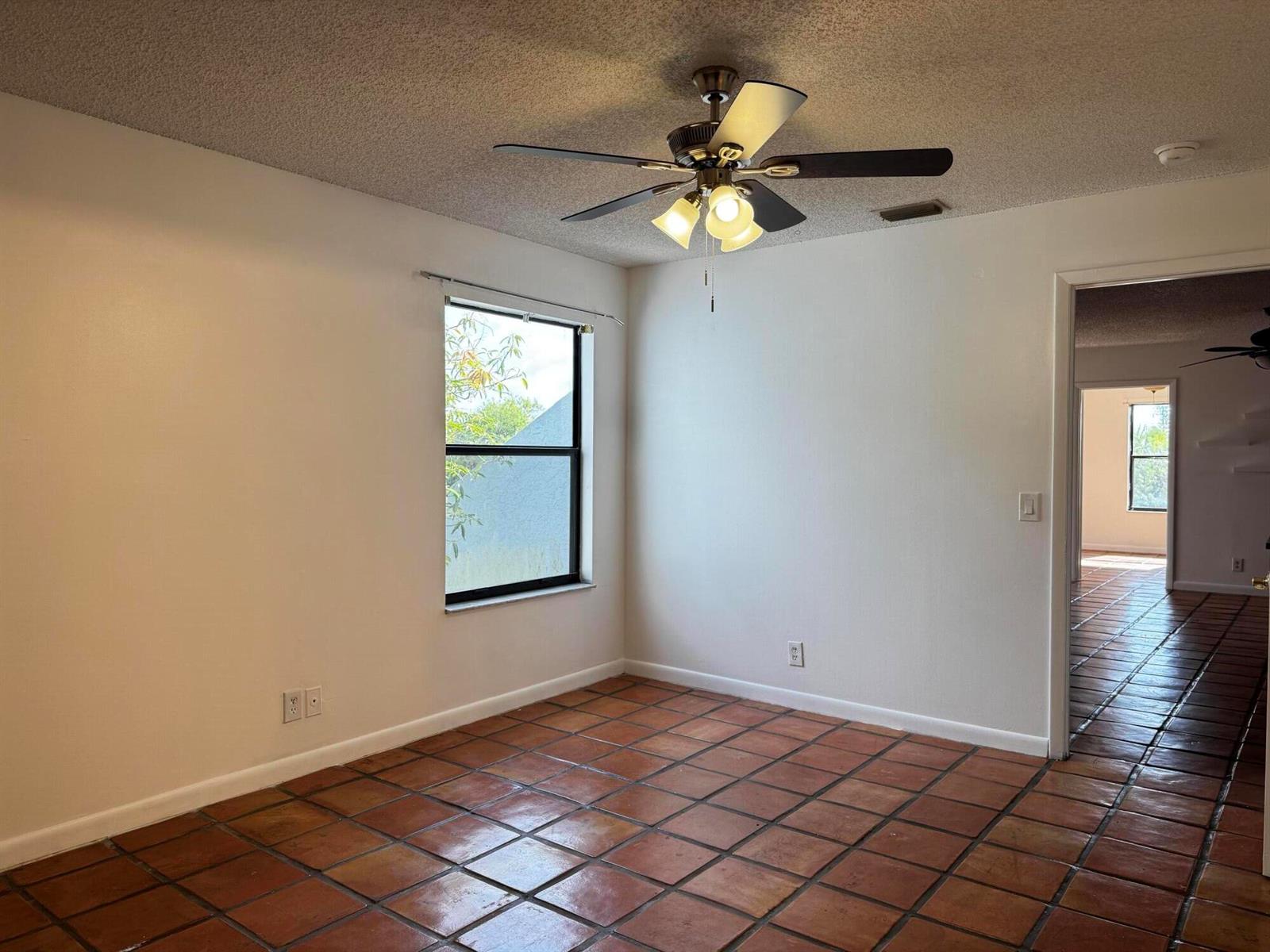 An empty room features terracotta tile flooring, white walls, a ceiling fan, and a window — 24 Crossings Circle # H, Boynton Beach FL 33435, BOYNTON BEACH, FL
