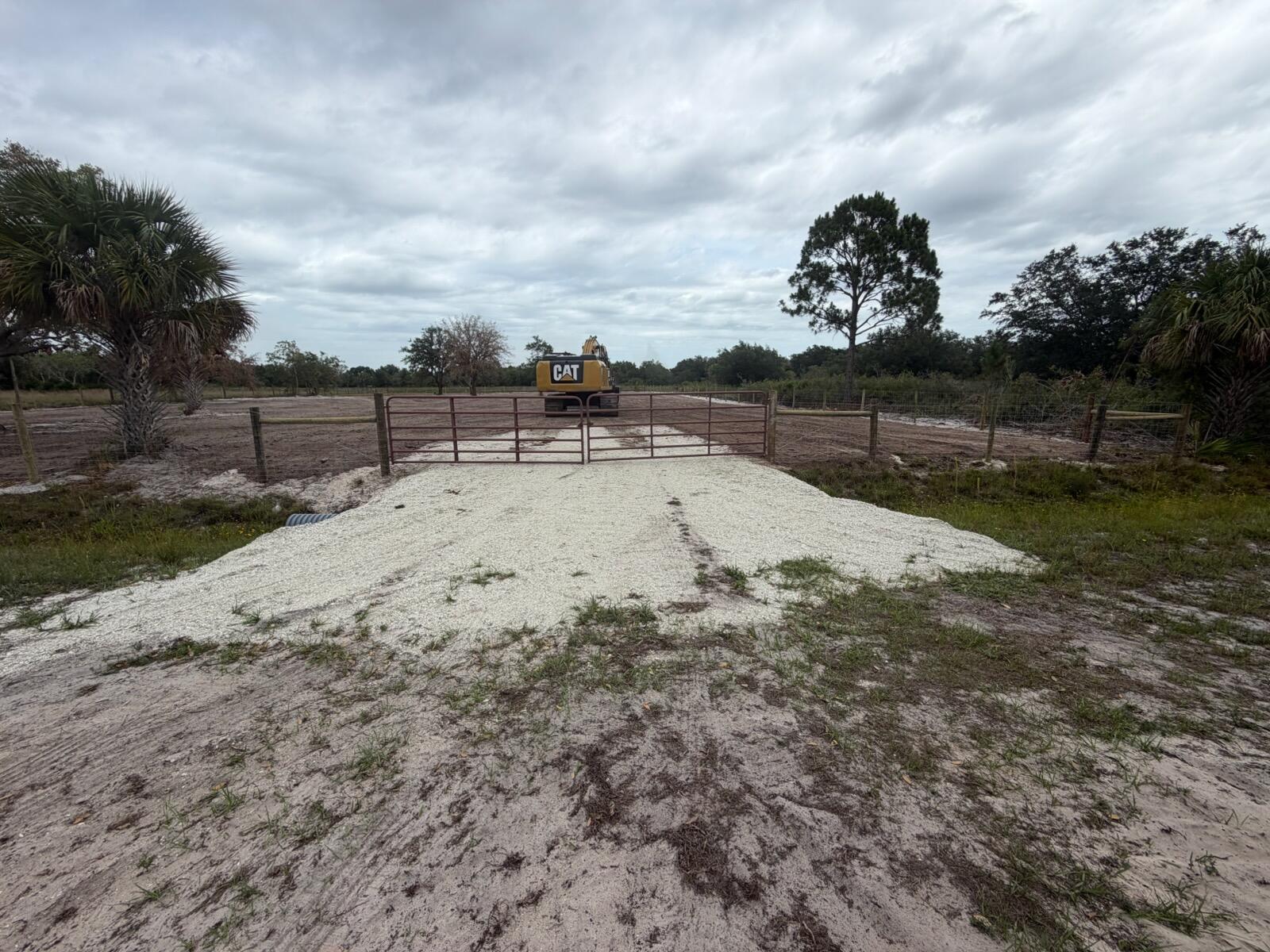 A gravel driveway leads to a metal gate opening into a cleared, fenced rural lot — 14667 NW 310th Street, Okeechobee FL 34972, OKEECHOBEE, FL