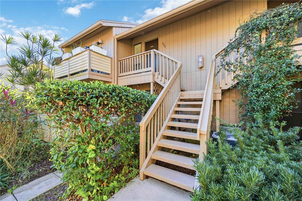 An exterior view of a two-story building with wooden stairs leading to an upper balcony — 1626 BROOKHOUSE DRIVE UNIT 235, SARASOTA, FL