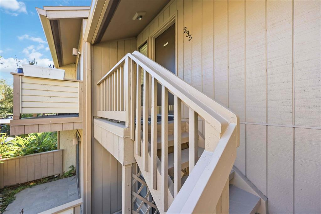 An exterior view of a tan building showing a staircase leading to an apartment entrance — 1626 BROOKHOUSE DRIVE UNIT 235, SARASOTA, FL