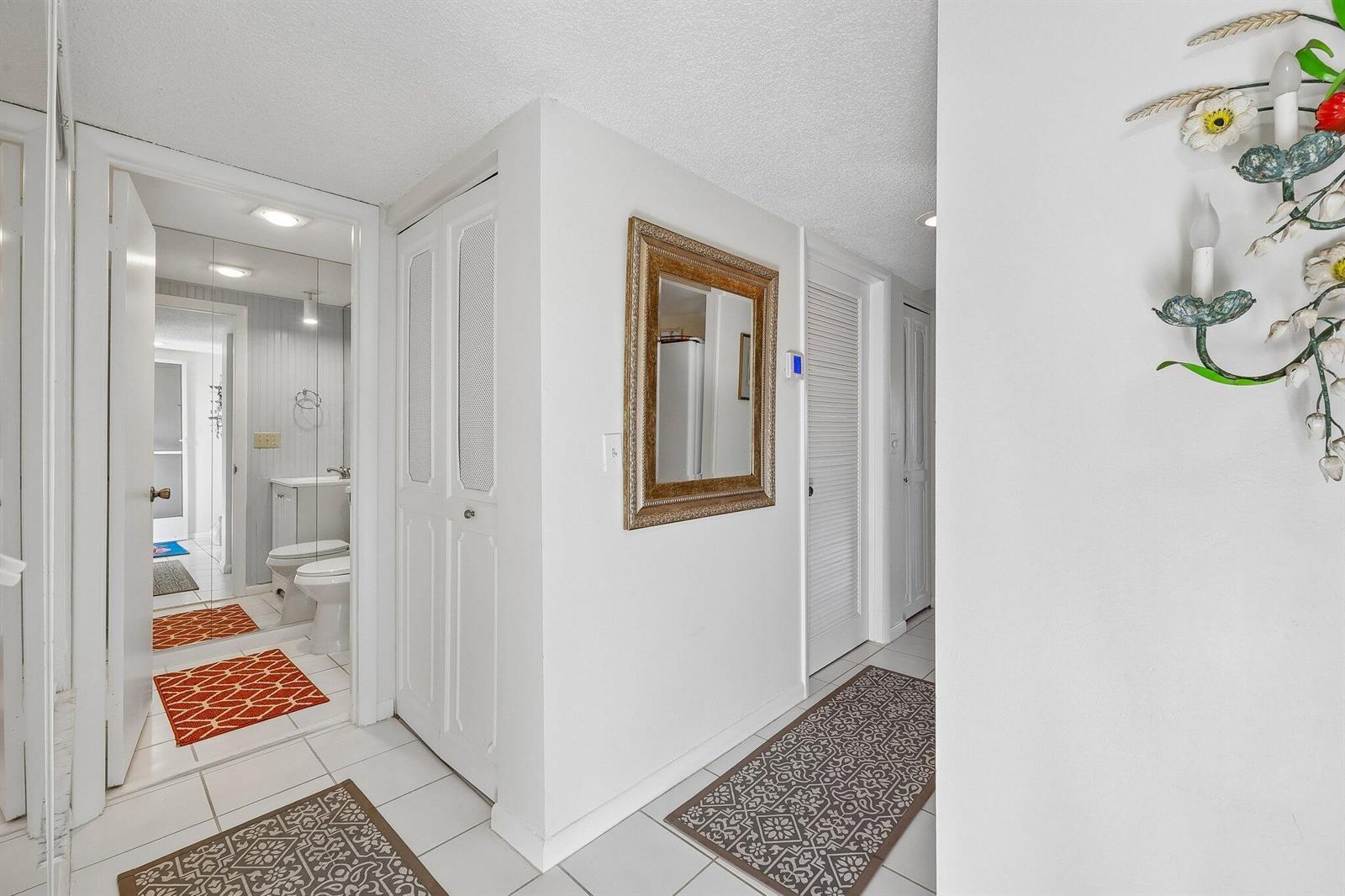 A white hallway features a bathroom entrance, louvered closet doors, a mirror, and tiled floors — 9240 SE Riverfront # D, Jupiter FL 33469, JUPITER, FL
