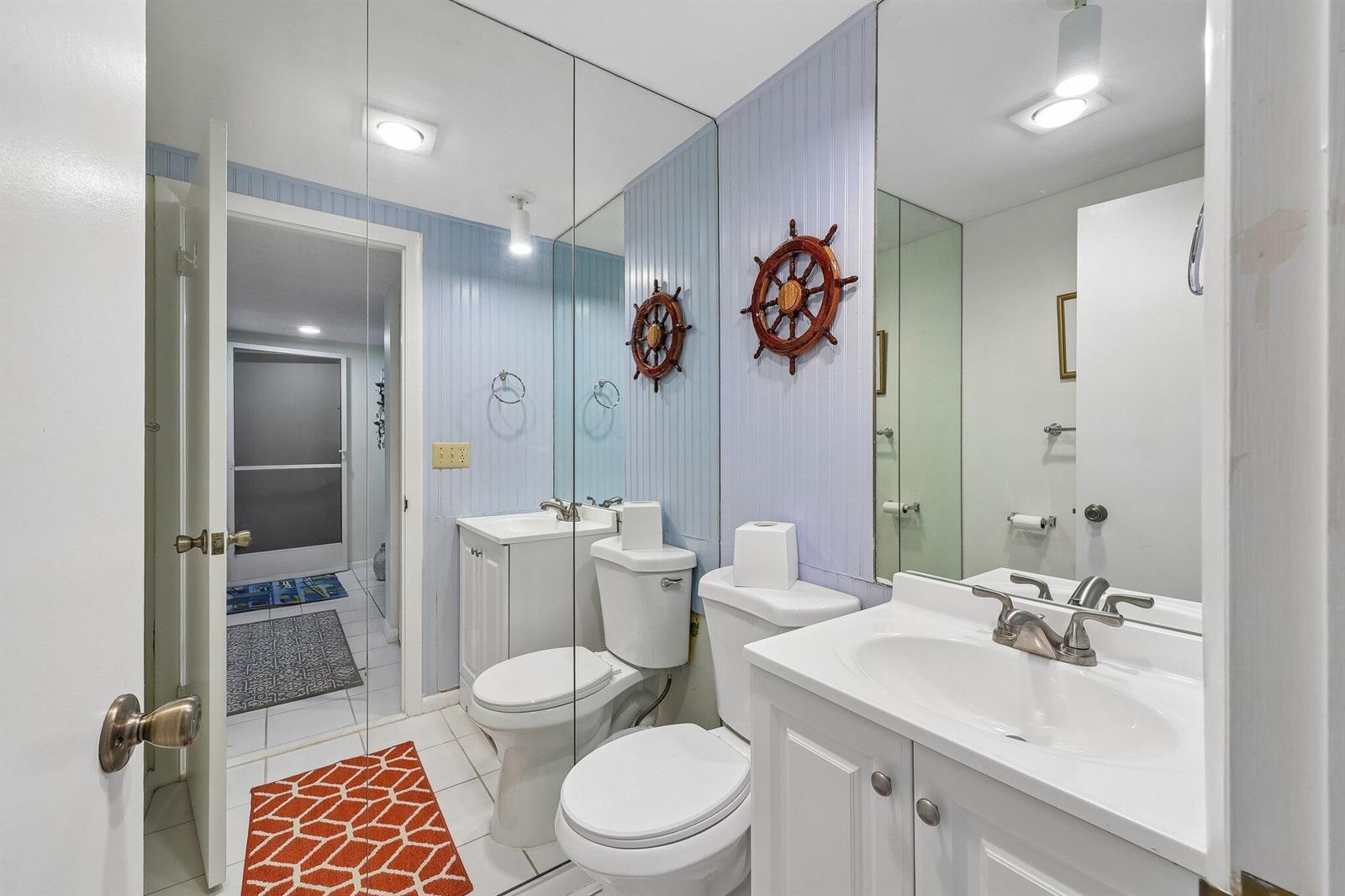 A bathroom features a white vanity, a toilet, and light blue beadboard walls with mirrors — 9240 SE Riverfront # D, Jupiter FL 33469, JUPITER, FL