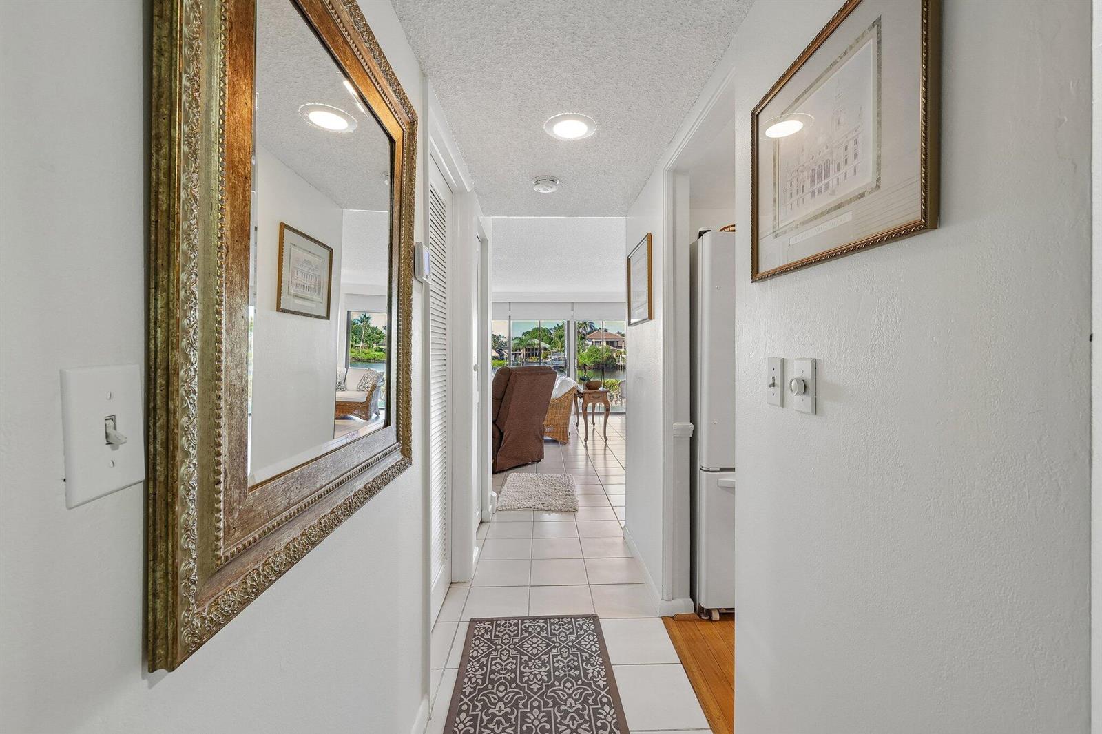A hallway with white tile floors leads toward a bright living area with water views — 9240 SE Riverfront # D, Jupiter FL 33469, JUPITER, FL