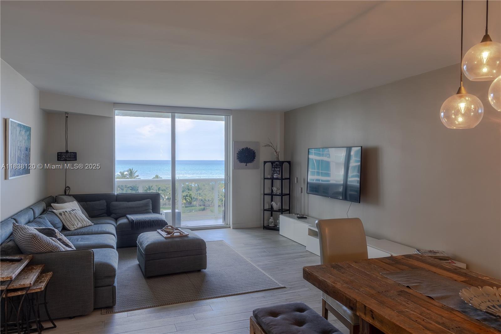 A living room features a grey sectional sofa, a television, and a balcony with ocean views — 10275 Collins Ave # 634, Bal Harbour FL 33154, BAL HARBOUR, FL