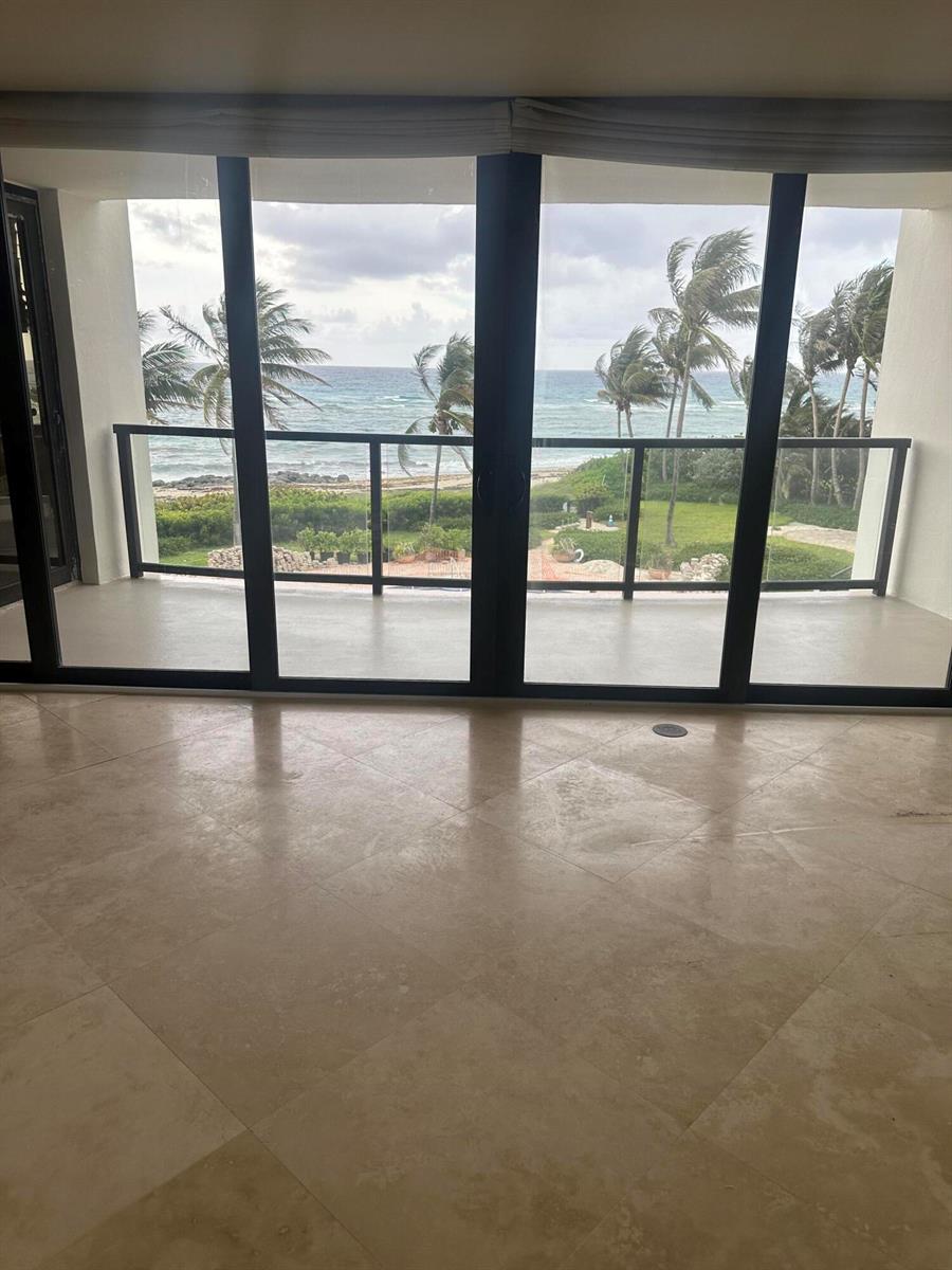 A room with large glass sliding doors overlooking a balcony, palm trees, and the ocean — 6885 N Ocean Boulevard # 3040, Ocean Ridge FL 33435, OCEAN RIDGE, FL