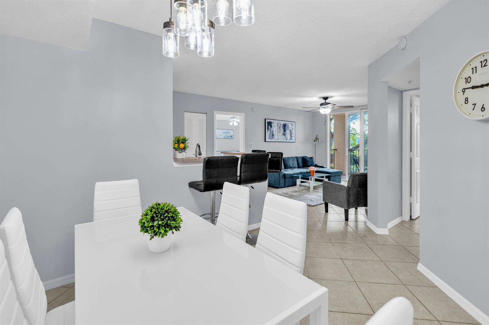 A dining area with a white table and chairs overlooks a living room and balcony — 214 Villa Circle # 214, Boynton Beach FL 33435, BOYNTON BEACH, FL