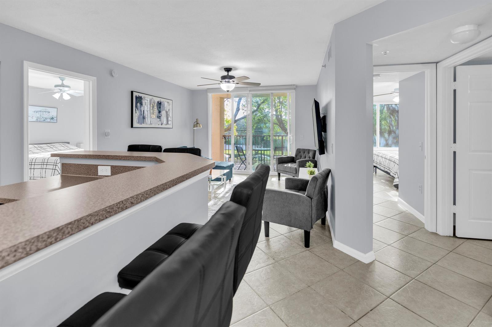 A living room with a breakfast bar, gray armchairs, and a sliding door to a balcony — 214 Villa Circle # 214, Boynton Beach FL 33435, BOYNTON BEACH, FL