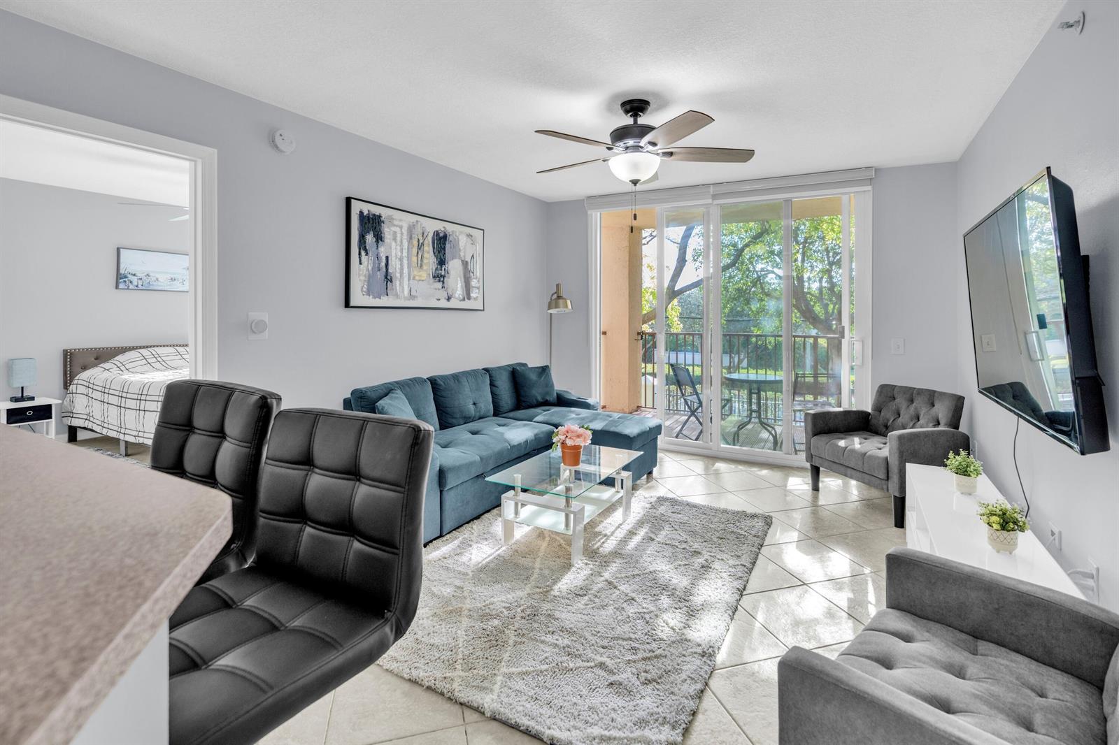 A living room features a blue sectional sofa, gray armchairs, and a sliding glass door — 214 Villa Circle # 214, Boynton Beach FL 33435, BOYNTON BEACH, FL
