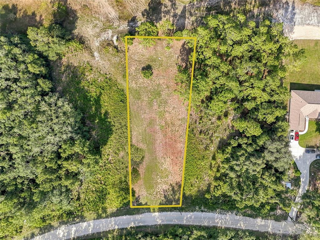 An aerial view shows a vacant, trapezoidal-shaped lot outlined in yellow near a paved road — 100 BERRYHILL DRIVE, WEBSTER, FL