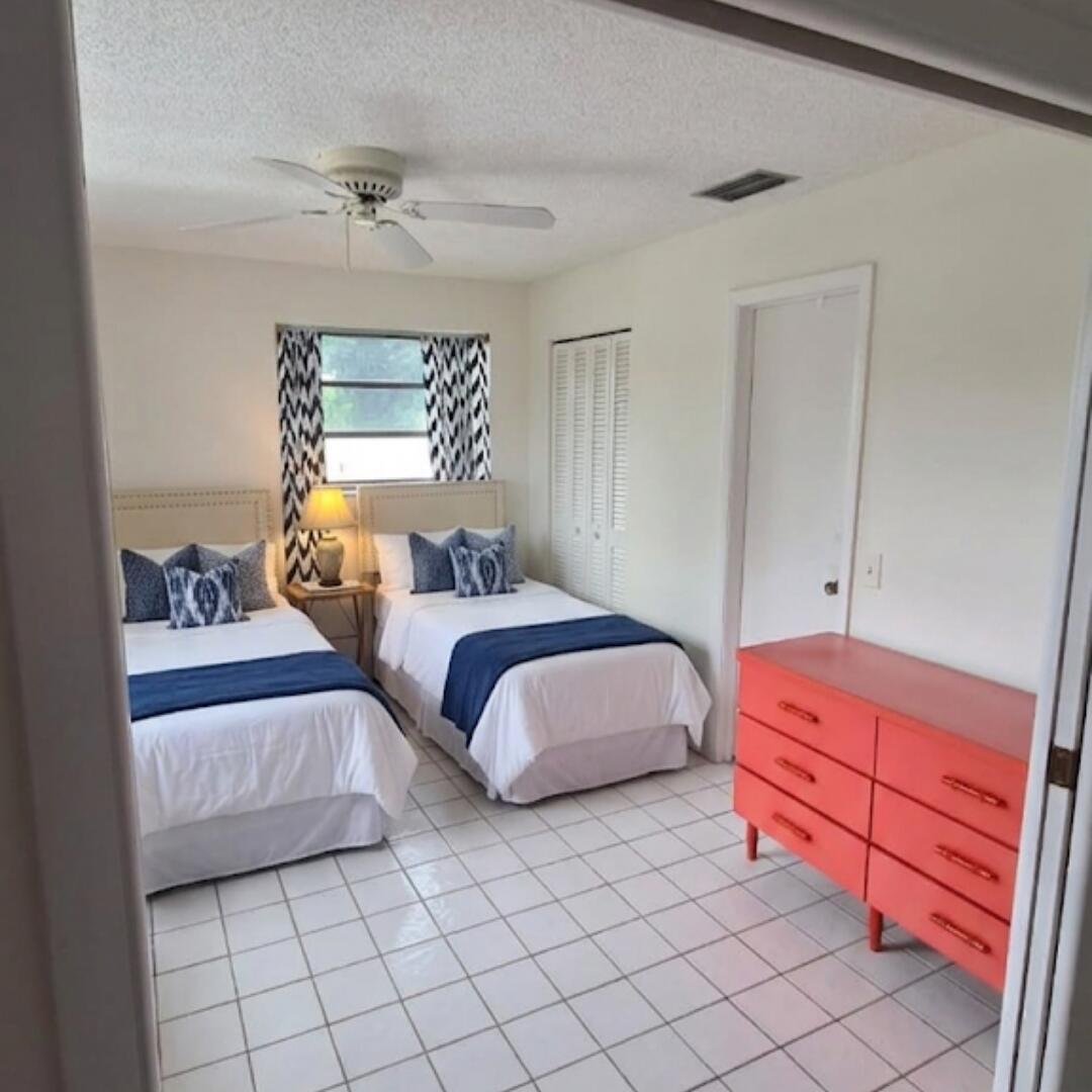 A bedroom features two twin beds, white tile flooring, and a coral-colored dresser — 13746 Via Flora, Delray Beach FL 33484, DELRAY BEACH, FL