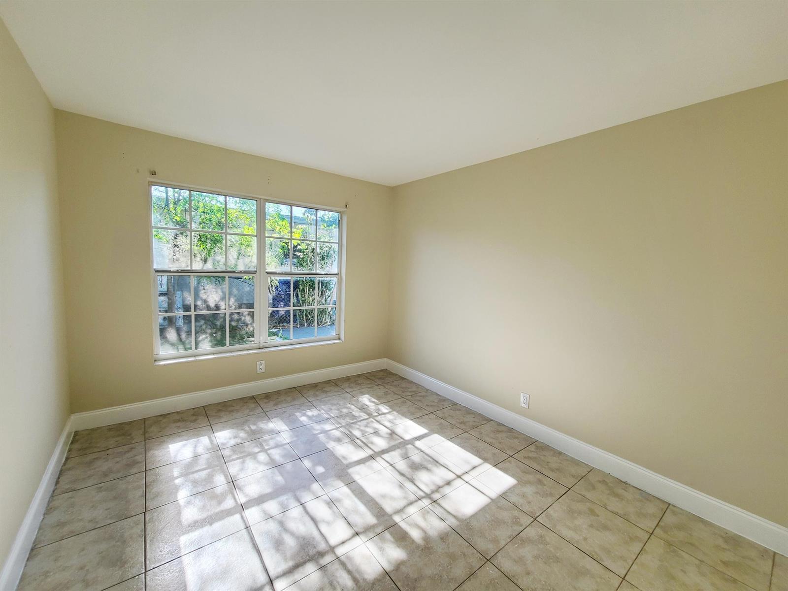 An empty room with beige walls, tile flooring, and a large window with grid panes — 420 Blue Heron Boulevard # 2, West Palm Beach FL 33404, WEST PALM BEACH, FL