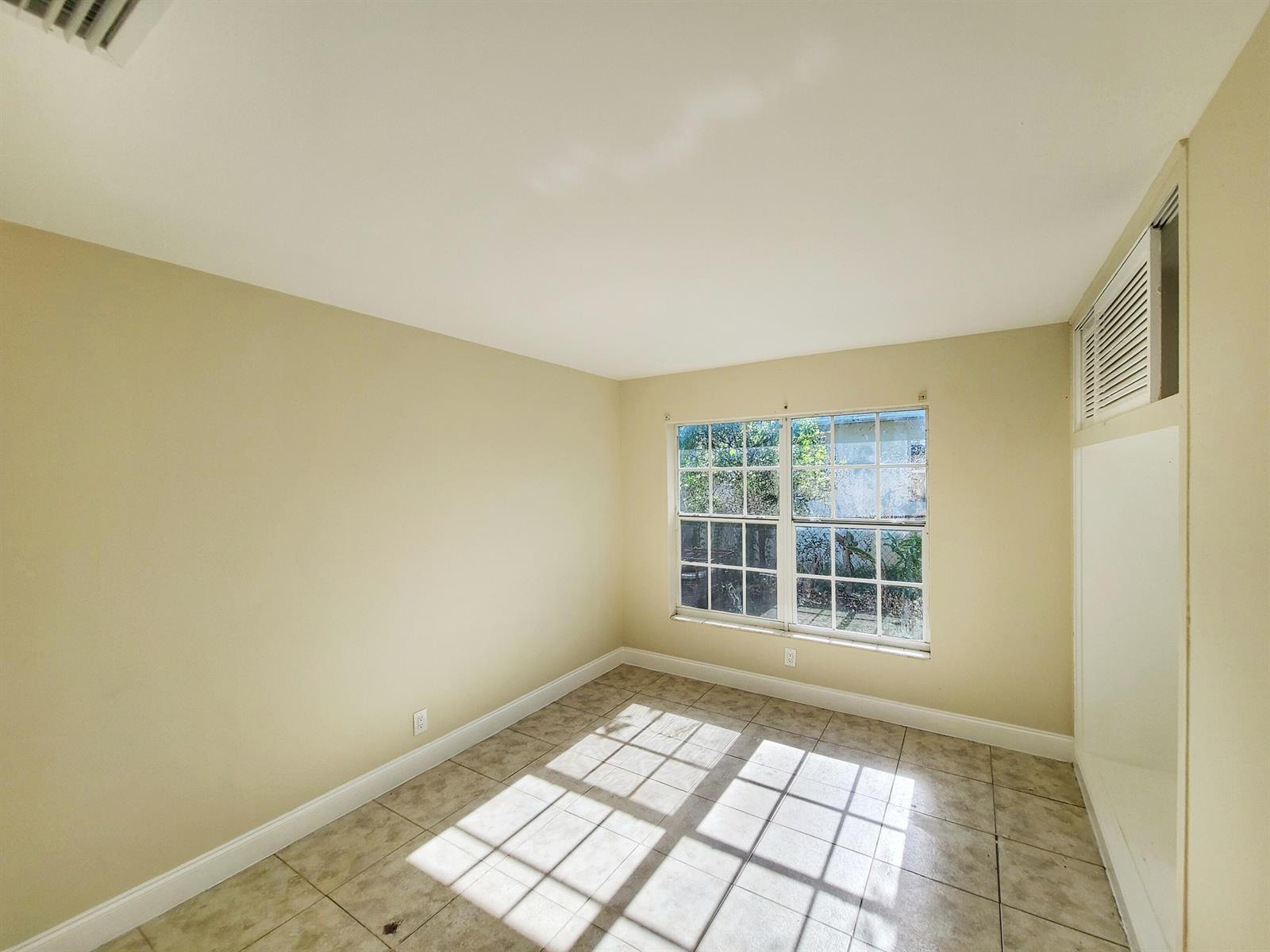 An empty room with beige walls, tile flooring, and a window looking out to greenery — 420 Blue Heron Boulevard # 2, West Palm Beach FL 33404, WEST PALM BEACH, FL