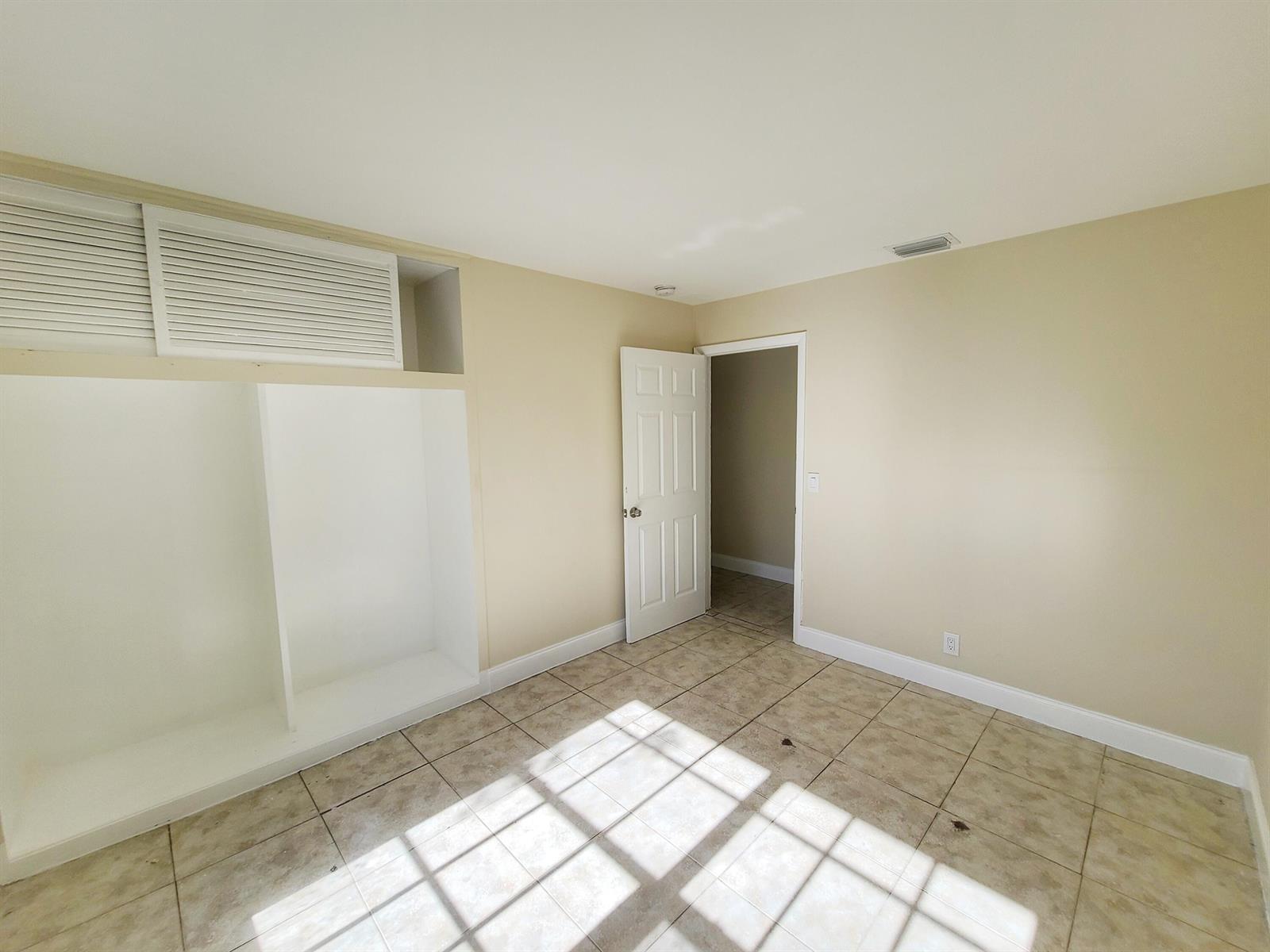 An empty room with beige walls, tile flooring, a built-in shelving unit, and an open doorway — 420 Blue Heron Boulevard # 2, West Palm Beach FL 33404, WEST PALM BEACH, FL