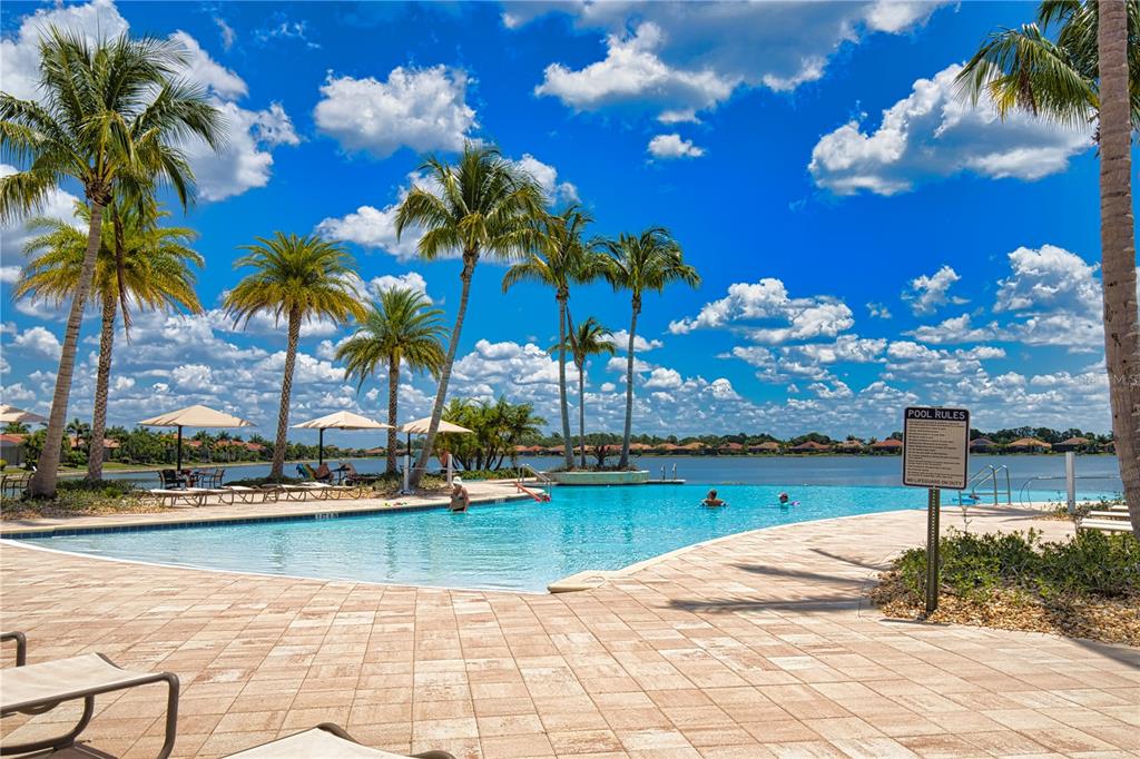 A swimming pool with palm trees and umbrellas overlooks a lake under a blue sky — 104 VILLORESI BOULEVARD, NOKOMIS, FL