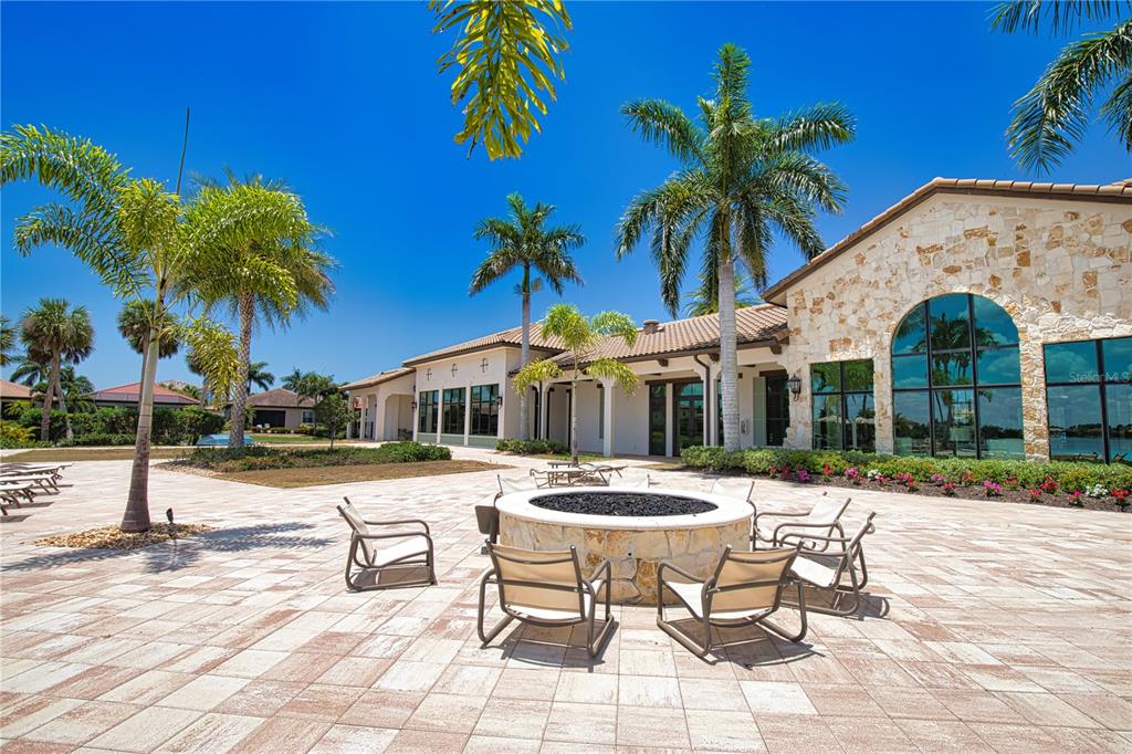 A stone fire pit with patio chairs sits on a paved terrace outside a building — 104 VILLORESI BOULEVARD, NOKOMIS, FL
