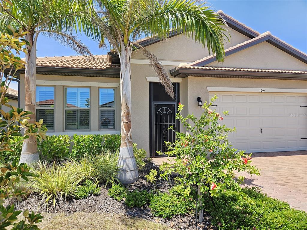 The exterior of a single-story house features a tan stucco facade, palm trees, and a garage — 104 VILLORESI BOULEVARD, NOKOMIS, FL