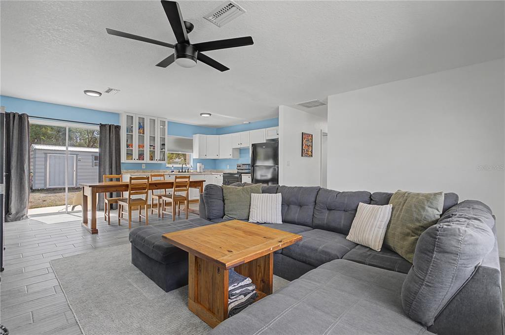 A living room with a gray sectional sofa opens to a kitchen and dining area — 17235 URSULA AVENUE, PORT CHARLOTTE, FL