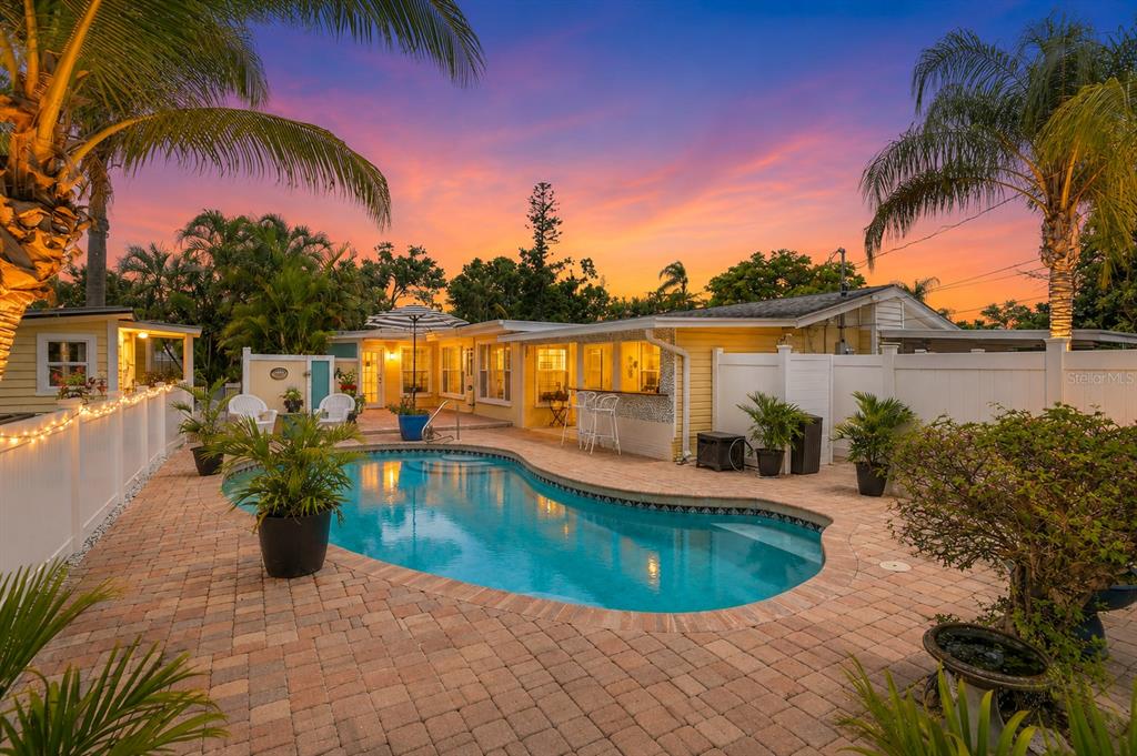 A backyard features a swimming pool surrounded by brick pavers and a yellow house exterior — 2403 VERMONT AVENUE E, BRADENTON, FL
