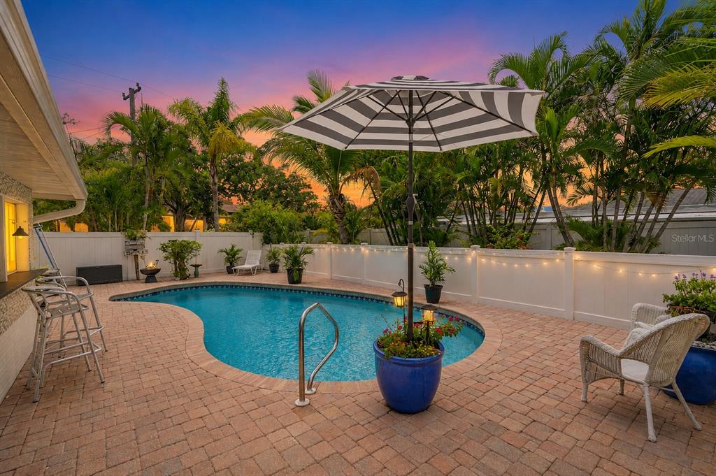 A backyard swimming pool with a patio, umbrella, and white fence at sunset — 2403 VERMONT AVENUE E, BRADENTON, FL