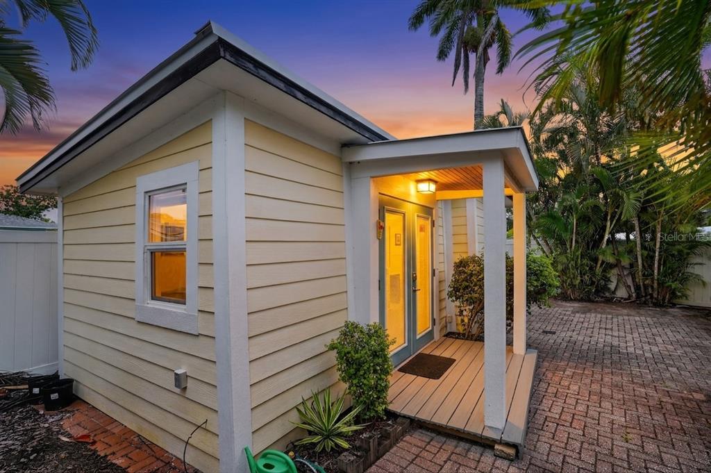 A small yellow cottage with a covered porch and glass doors sits on a brick patio — 2403 VERMONT AVENUE E, BRADENTON, FL