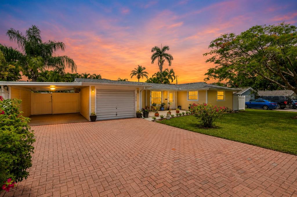A yellow single-story house with a brick driveway and a carport at sunset — 2403 VERMONT AVENUE E, BRADENTON, FL
