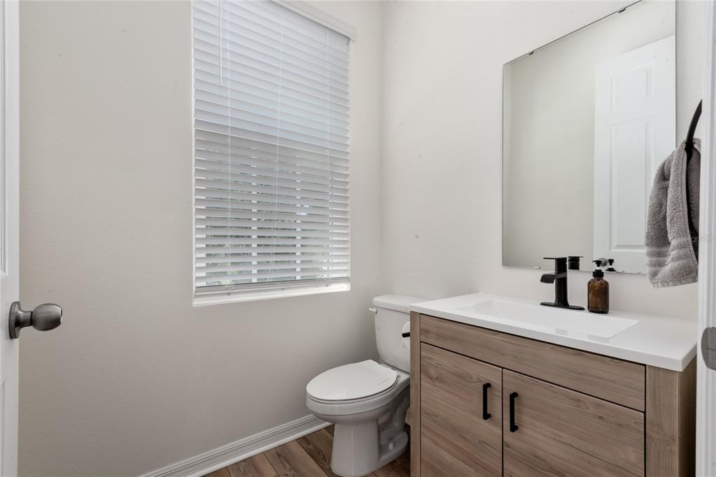 A small bathroom features a wood-finish vanity, a white toilet, and a window with blinds — 2101 CELEBRATION BOULEVARD, KISSIMMEE, FL