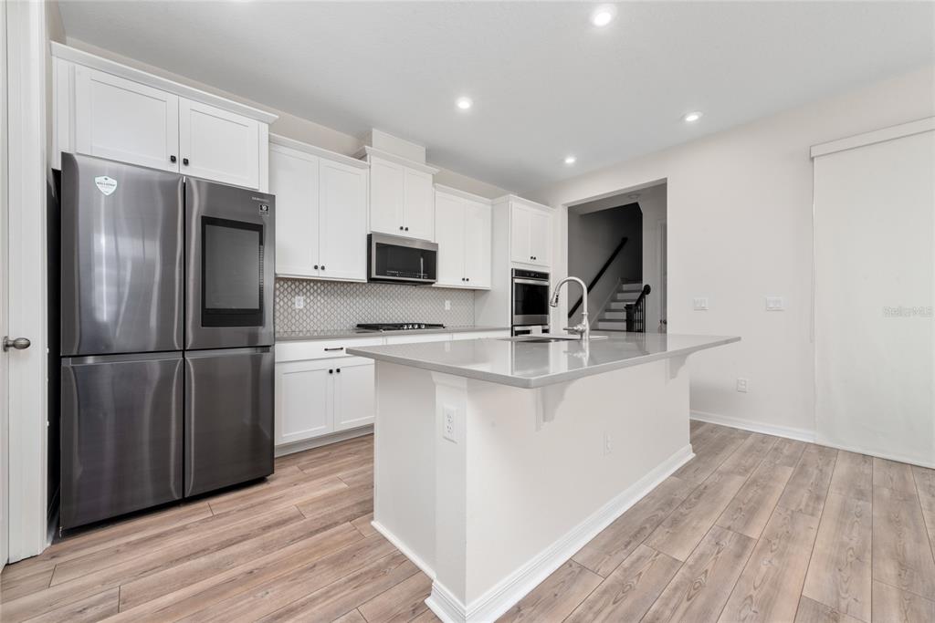 A modern kitchen features white cabinets, stainless steel appliances, a gray island, and wood flooring — 2101 CELEBRATION BOULEVARD, KISSIMMEE, FL