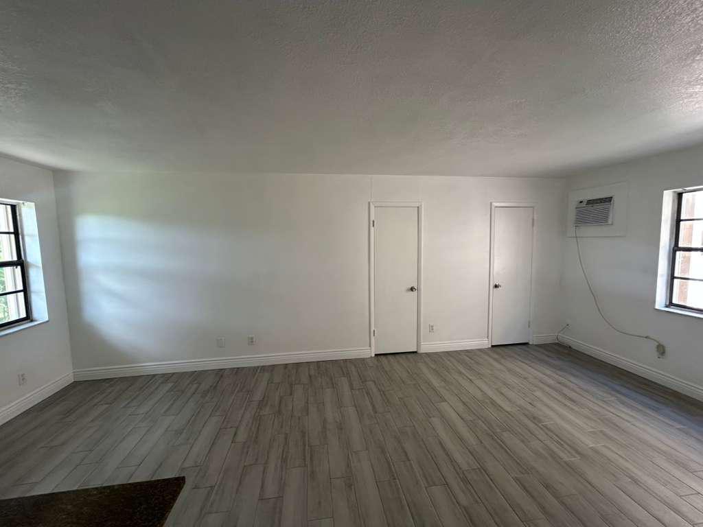 An empty room with white walls, gray wood-look tile flooring, two doors, and two windows — 1081 SE Monterey Road # 12, Stuart FL 34994, STUART, FL